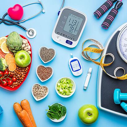 Gesunde Lebensmittel, Blutdruckmessgerät, Blutzuckermessgerät, Waage, Maßband, Hanteln und eine Wasserflasche sowie ein Stethoskop mit einem Herz.