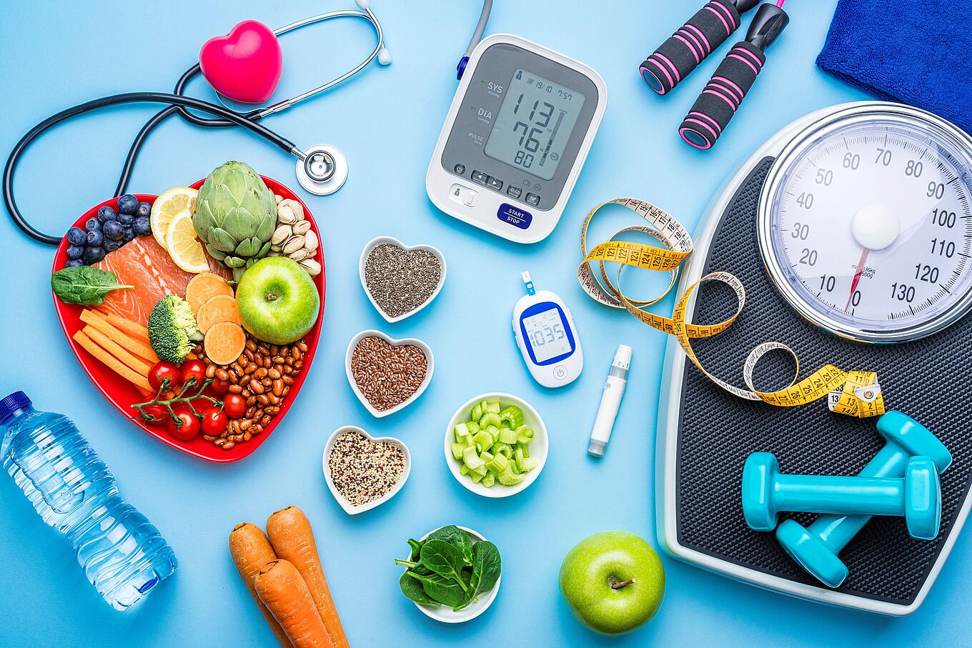 Gesunde Lebensmittel, Blutdruckmessgerät, Blutzuckermessgerät, Waage, Maßband, Hanteln und eine Wasserflasche sowie ein Stethoskop mit einem Herz.