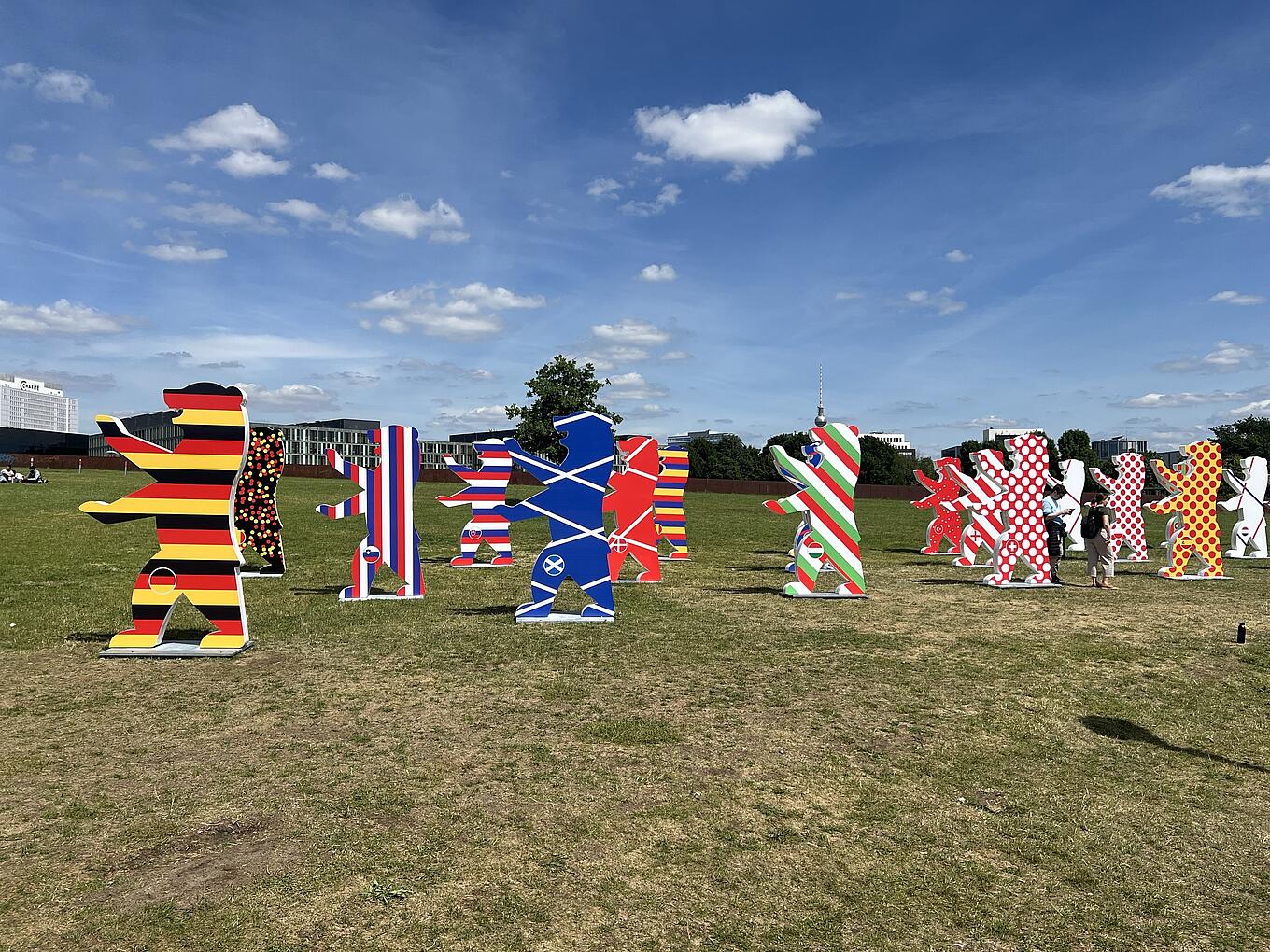17 Figuren des Berliner Bären stehen auf einer Wiese.