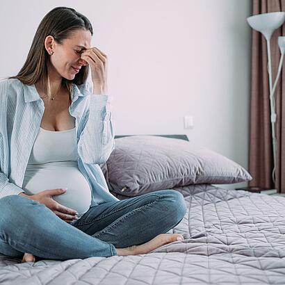 Schwangere Frau mit Kopfschmerzen auf dem Bett sitzend