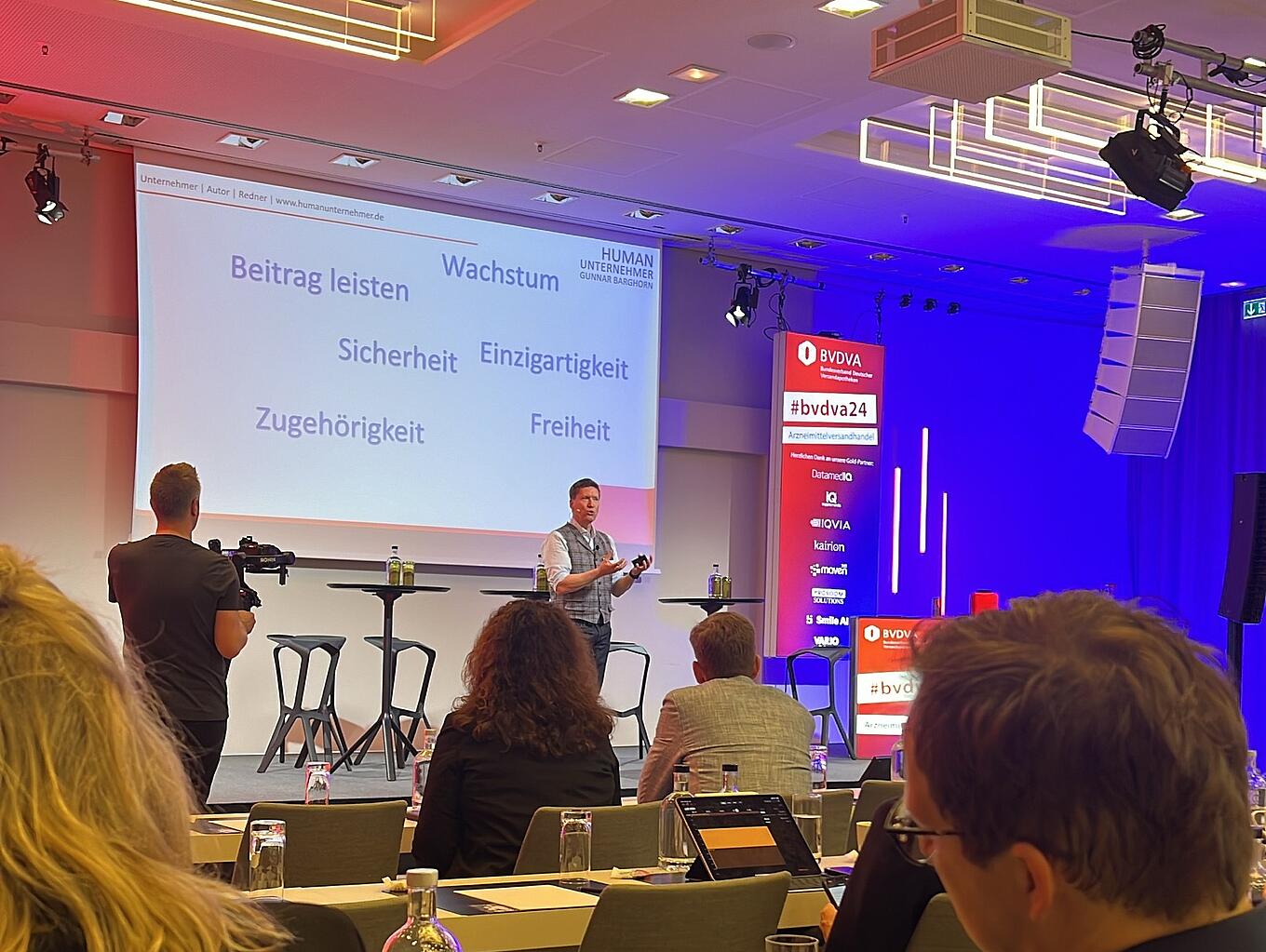 Beim BVDVA-Kongress 2024 spricht ein Mann auf einer Bühne in ein Mikrofon.