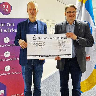 Juta-Pharma-Geschäftsführer Torben Jung Laursen und Schutzengel-Geschäftsführer Volker Syring halten einen großen symbolischen Check über 2.000 Euro für Schutzengel.