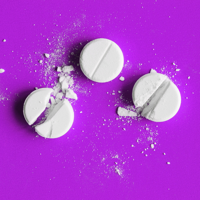 Eine ganze und zwei geteilte weiße Tabletten auf einem lila Hintergrund.