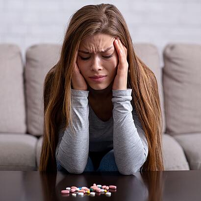 Frau mit Migräne vor verschiedenen Tabletten sitzend