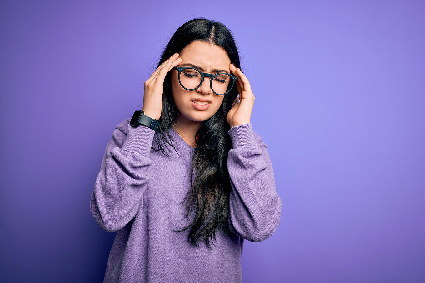 Eine Frau mit schmerzverzerrtem Gesicht fasst sich an den Kopf.