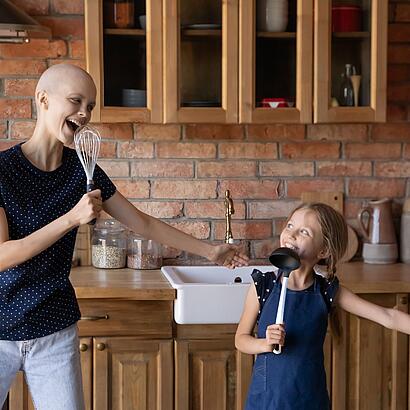 Eine Krebs-Erkrankte und ihre Tochter tanzen in der Küche.
