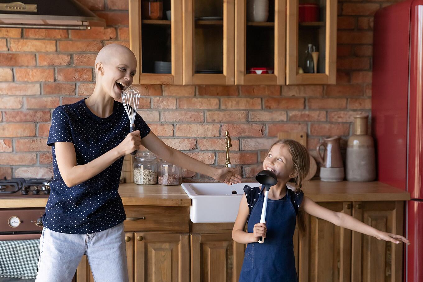 Eine Krebs-Erkrankte und ihre Tochter tanzen in der Küche.