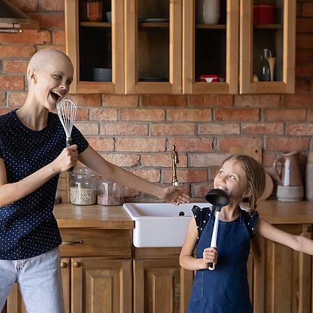 Eine Krebs-Erkrankte und ihre Tochter tanzen in der Küche.