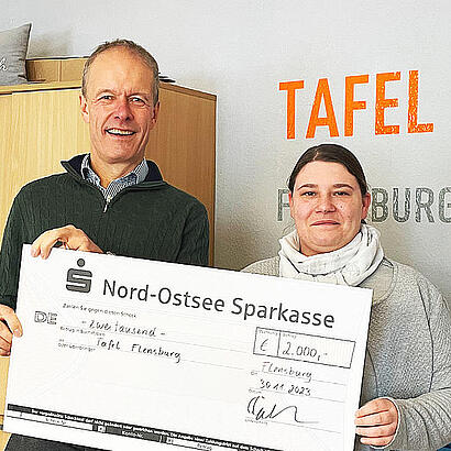 Geschäftsführer und Spendenempfänger halten einen Scheck in der Hand