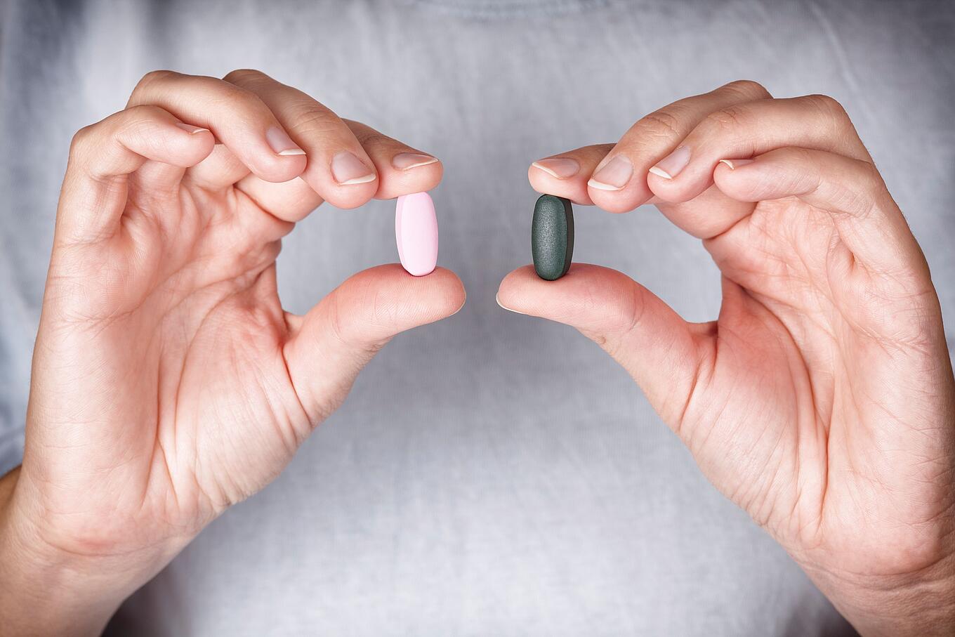 Zwei Hände zeigen zwei unterschiedliche farbende Tabletten