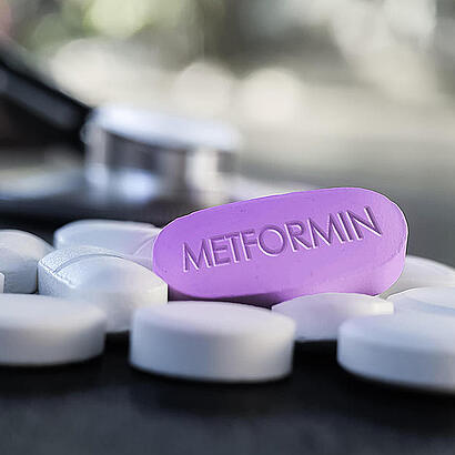 Lila Tablette mit "Metformin" Beschriftung zwischen weißen Tabletten.